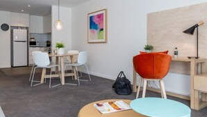 Una sala de estar moderna con comedor, una cocina al fondo y un cuadro abstracto grande en la pared.