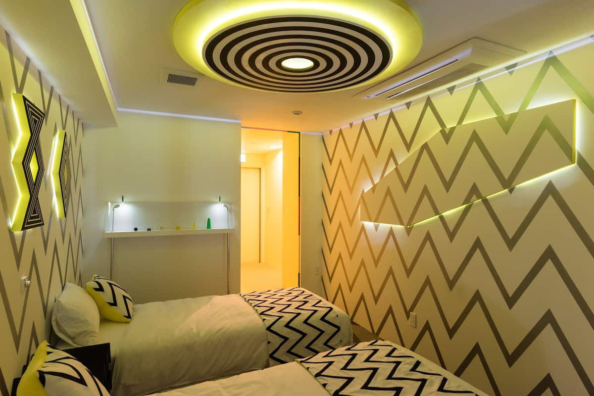 A modern hotel room with a geometric patterned wall, a circular ceiling light, and a bed with matching pillows.