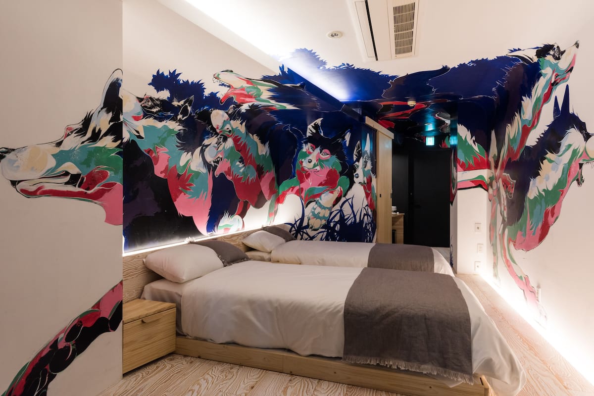 A modern bedroom with a large bed, a nightstand, and a wall mural.