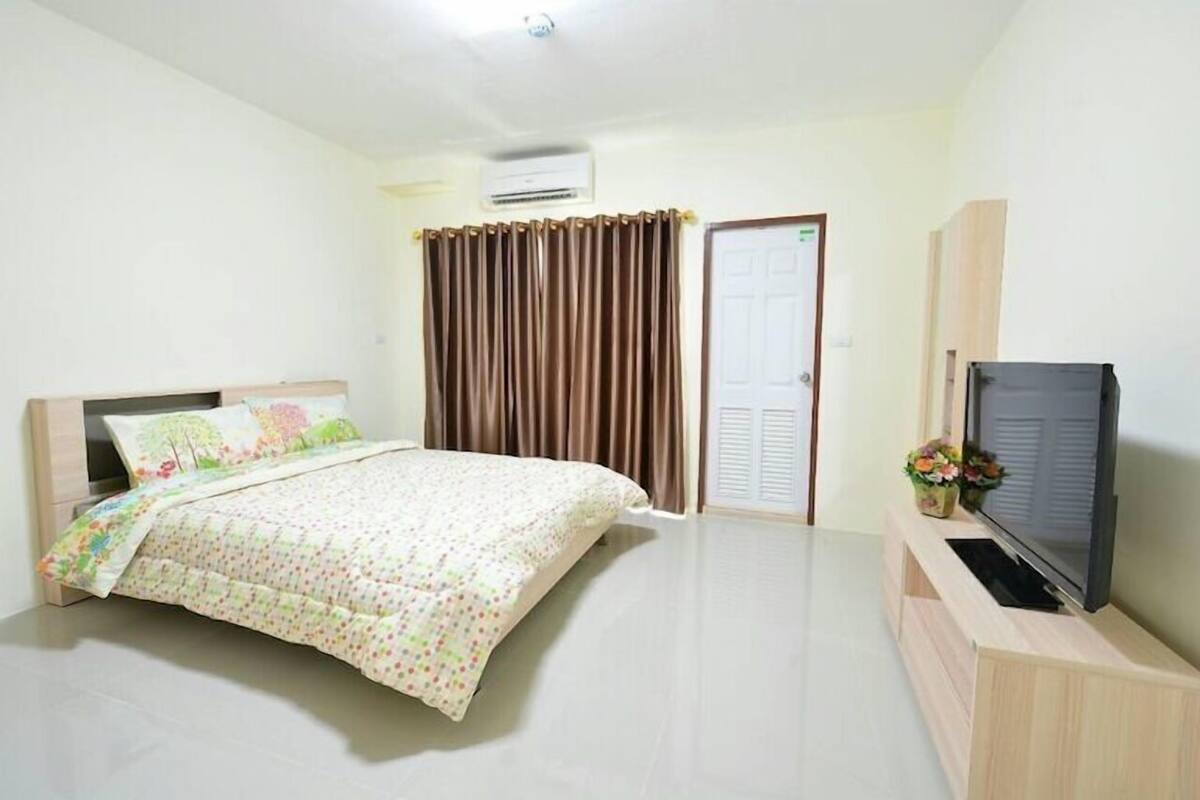 Un dormitorio con una cama, un televisor sobre un soporte de madera, una puerta y cortinas.