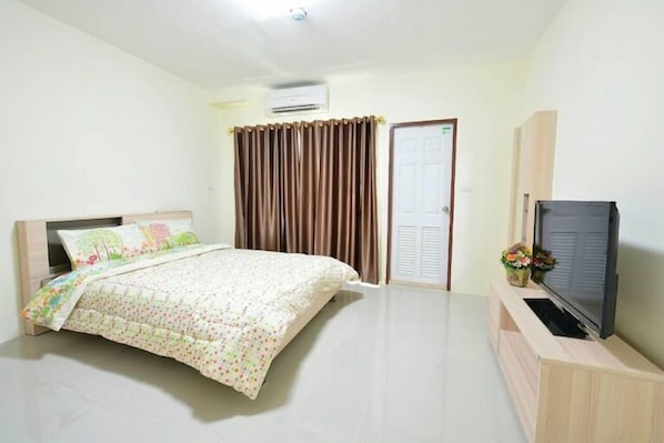 A bedroom with a bed, a TV on a wooden stand, a door, and curtains.