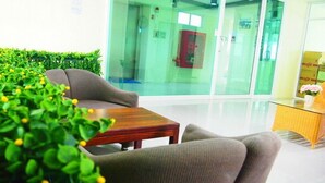 A reception area with a wooden table and two grey chairs, a glass wall, and a small potted plant. - 42 Place (Bangkok)