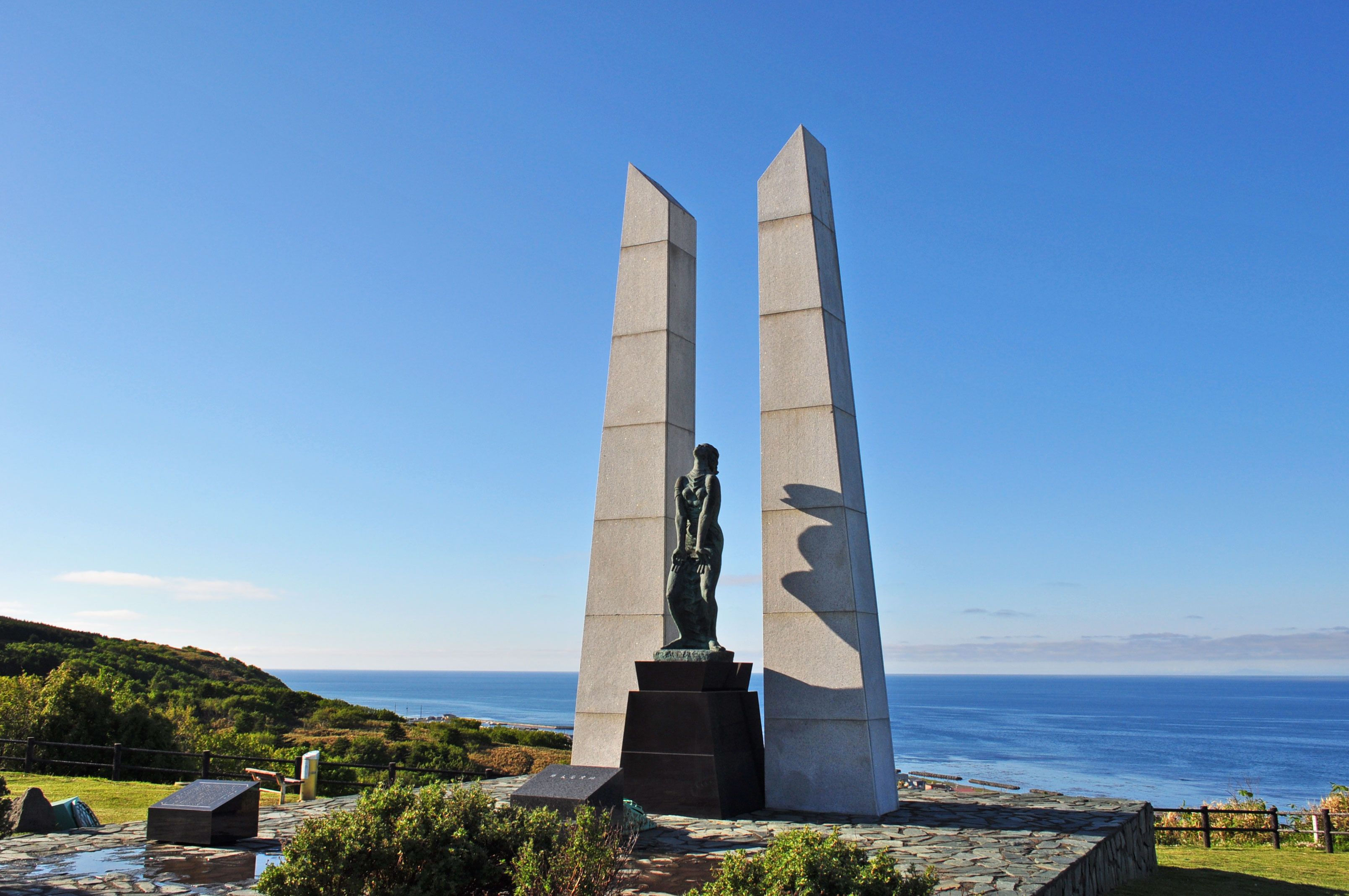 A monument with two tall pillars and a statue in the center, overlooking a coastal landscape.