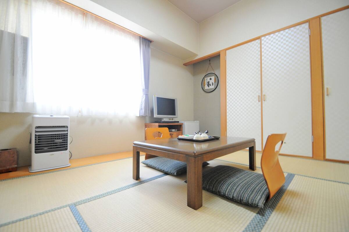 Perinteinen japanilainen huone, jossa on tatamimatto, matala pöytä, televisio ja liukuvat ovet.