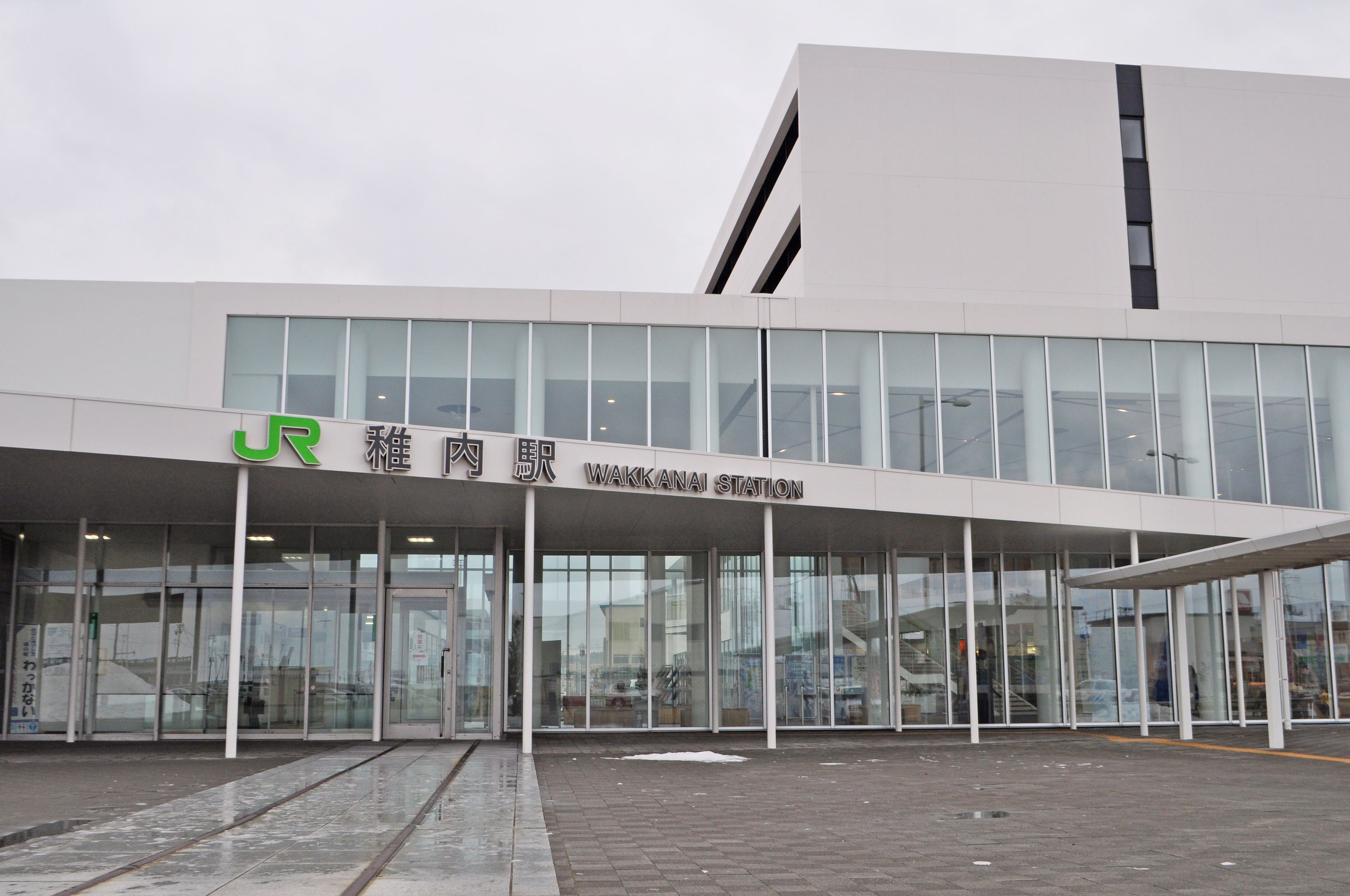 Ein modernes Gebäude mit Glasfassade und einem Schild, auf dem "WAKKANAI STATION" steht.