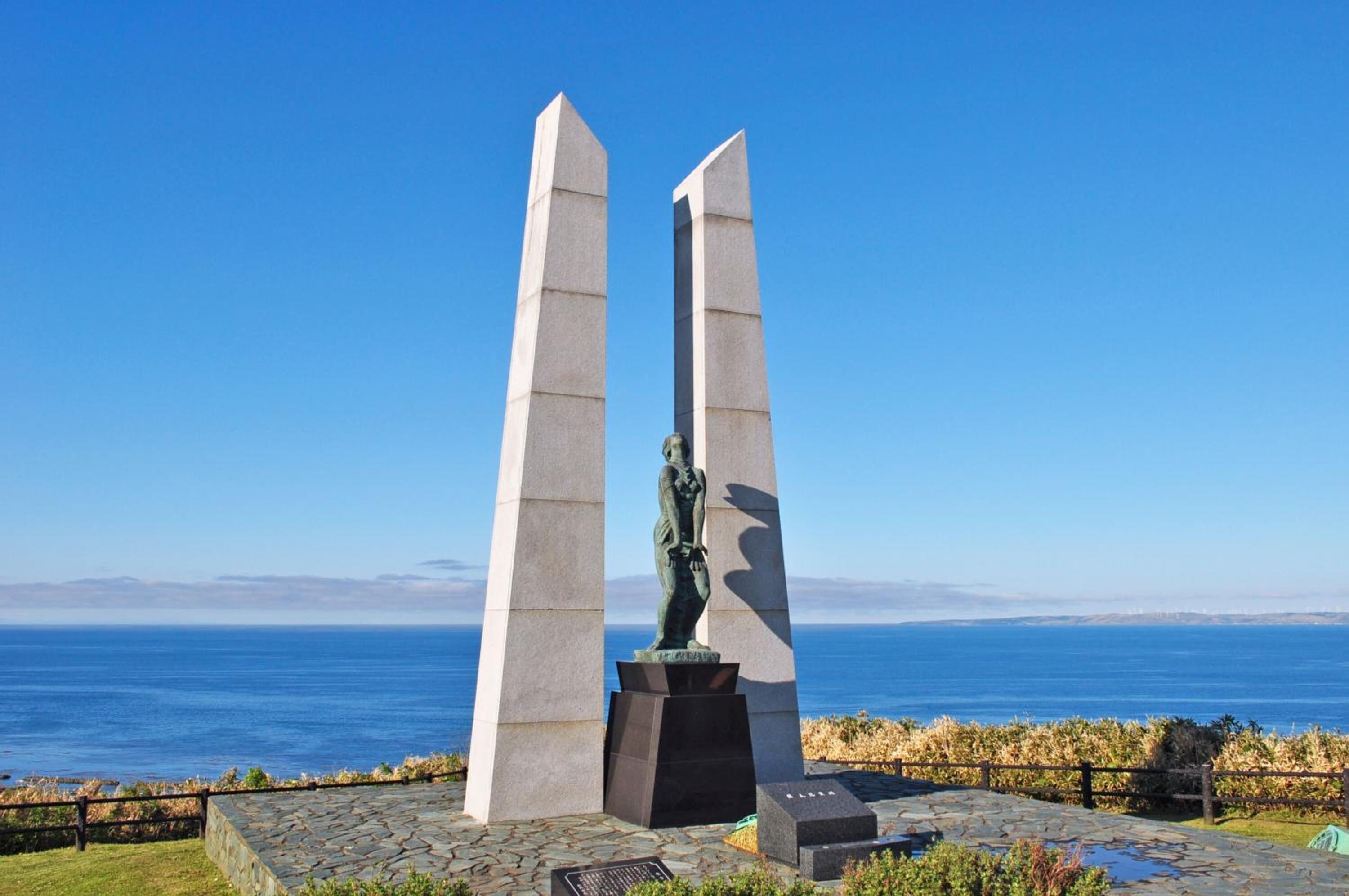 Un monumento con una estatua en el centro, dos altas columnas a cada lado y vista al océano en el fondo.