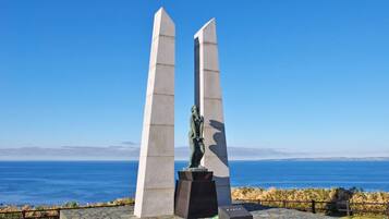 Un monumento con una estatua en el centro, dos altas columnas a cada lado y vista al océano en el fondo.