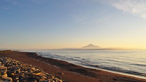 A beach with a rocky foreground, a sandy shore, and a mountain in the distance. - Hotel Saharin (Wakkanai)