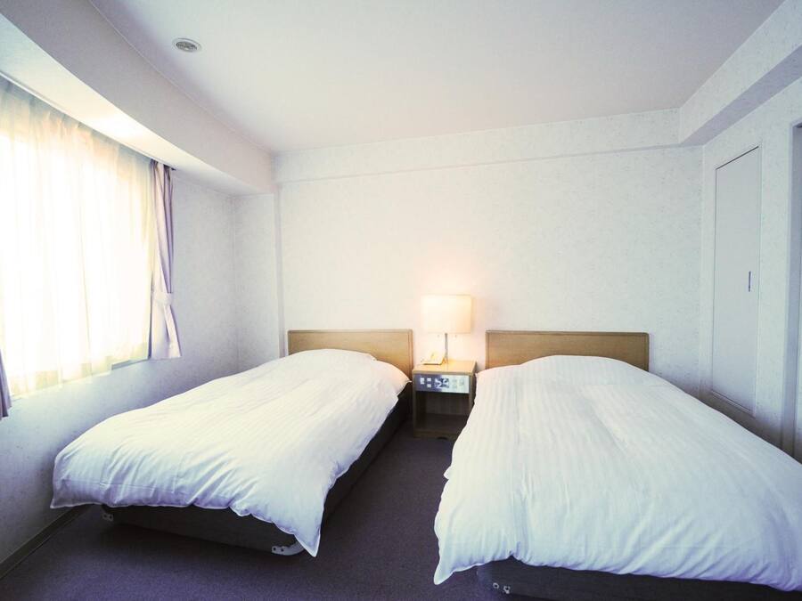 Une chambre d’hôtel avec deux lits simples, une table de chevet avec une lampe et une fenêtre avec des rideaux.