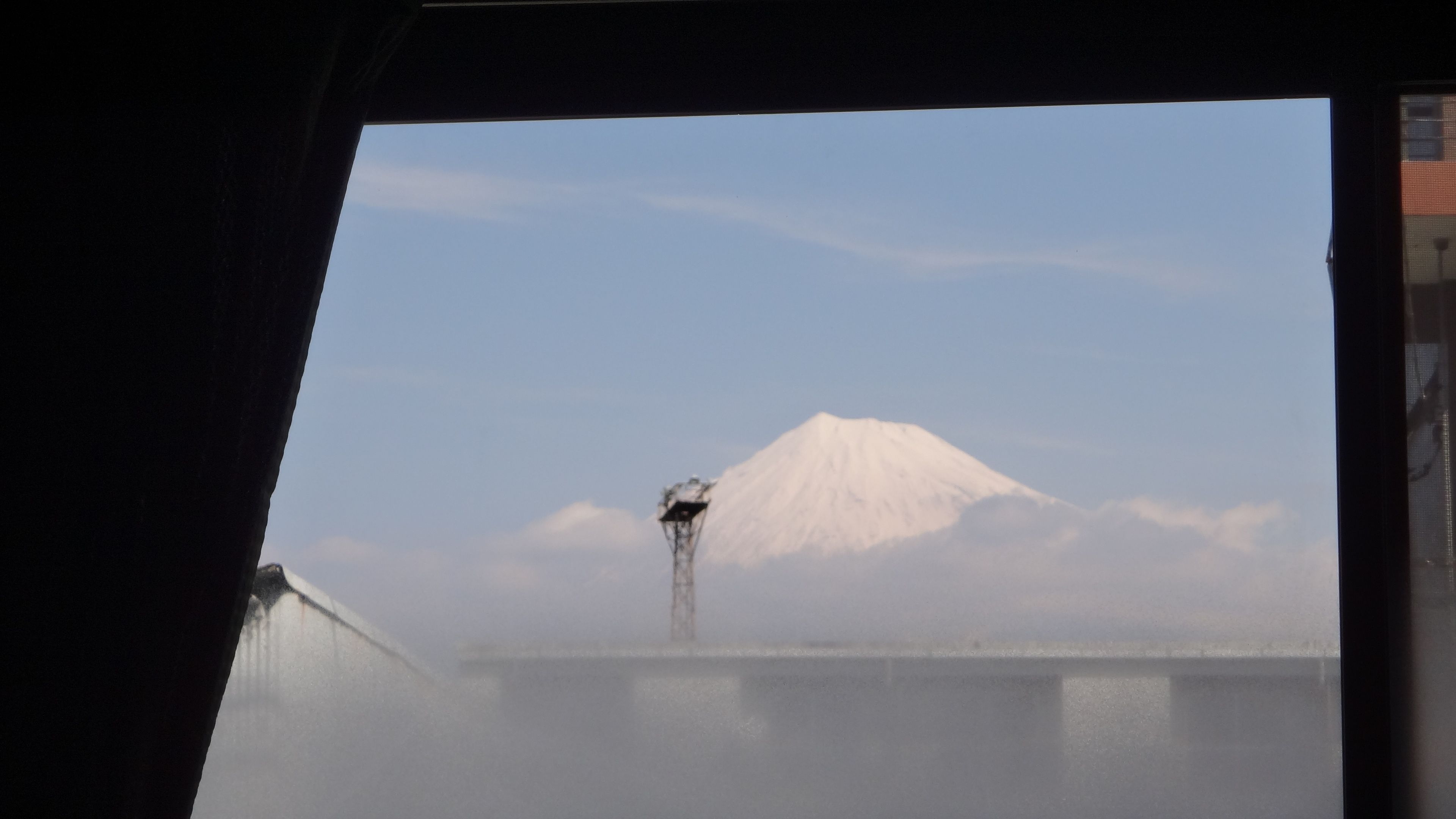 A view of a snow-capped mountain through a window with a metal structure in the foreground.