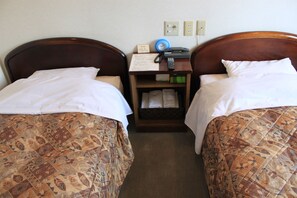 A hotel room with two beds, each with patterned bedding, a nightstand with a clock, a telephone, and a small table with a menu. - Hotel Hachimanzaka (Hakodate)