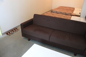 A brown sofa in a room with a carpeted floor and a small white table. - Hotel Hachimanzaka (Hakodate)