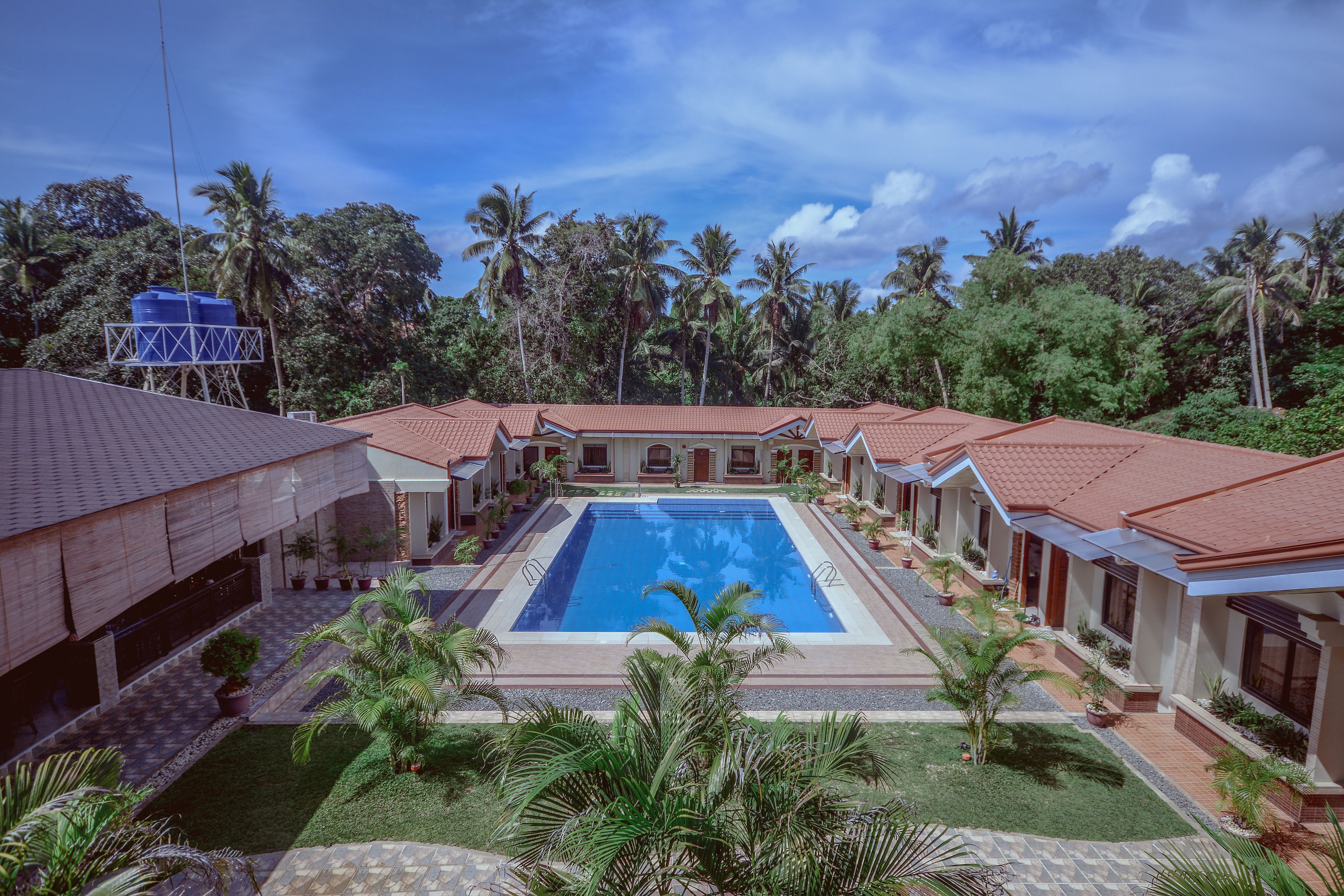 A resort with a central swimming pool, multiple guest rooms with red-tiled roofs, and lush greenery surrounding the property.