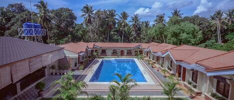 A resort with a central swimming pool, multiple guest rooms with red-tiled roofs, and lush greenery surrounding the property.