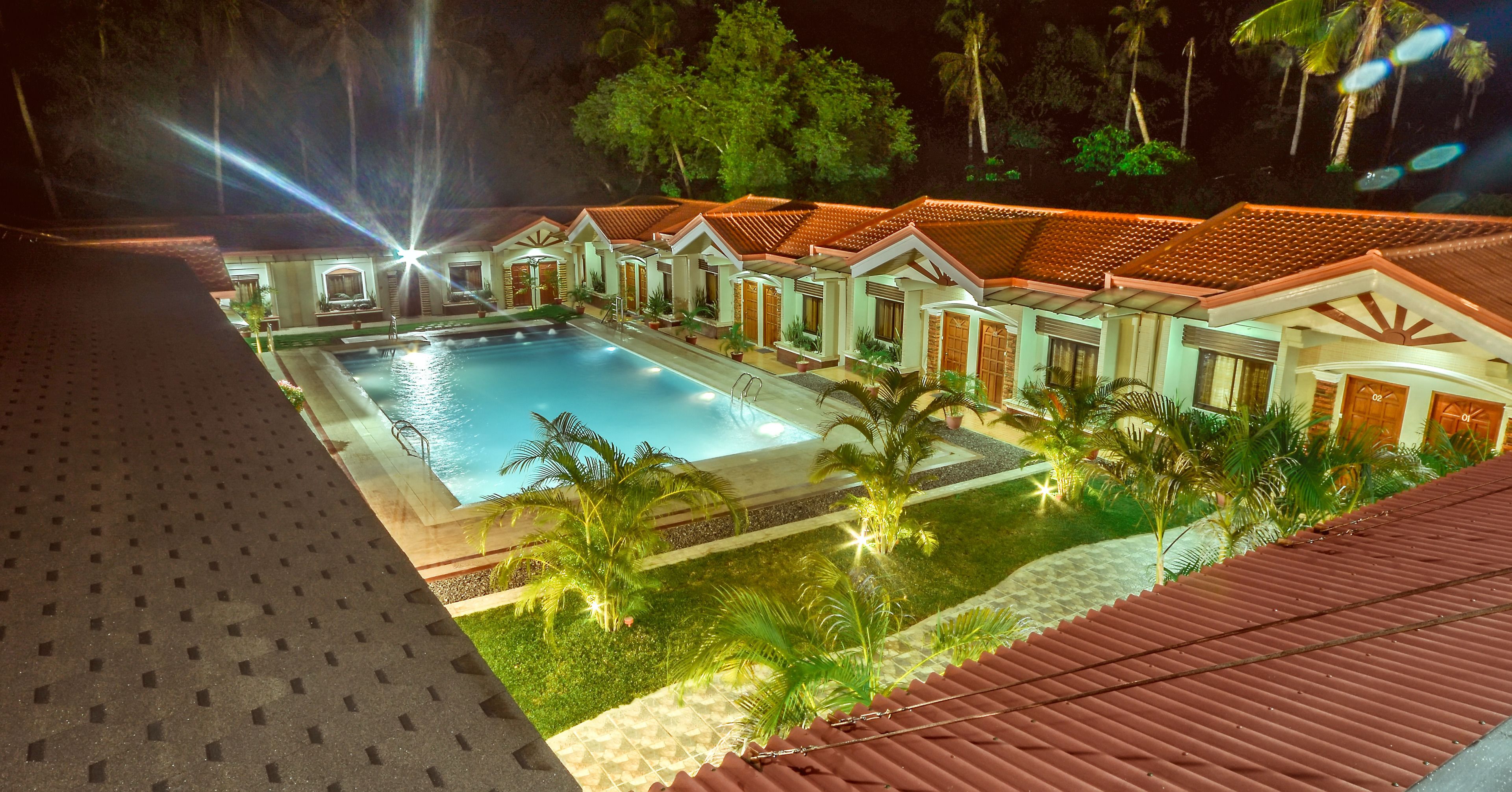 A hotel with a swimming pool, palm trees, and a red-roofed building.