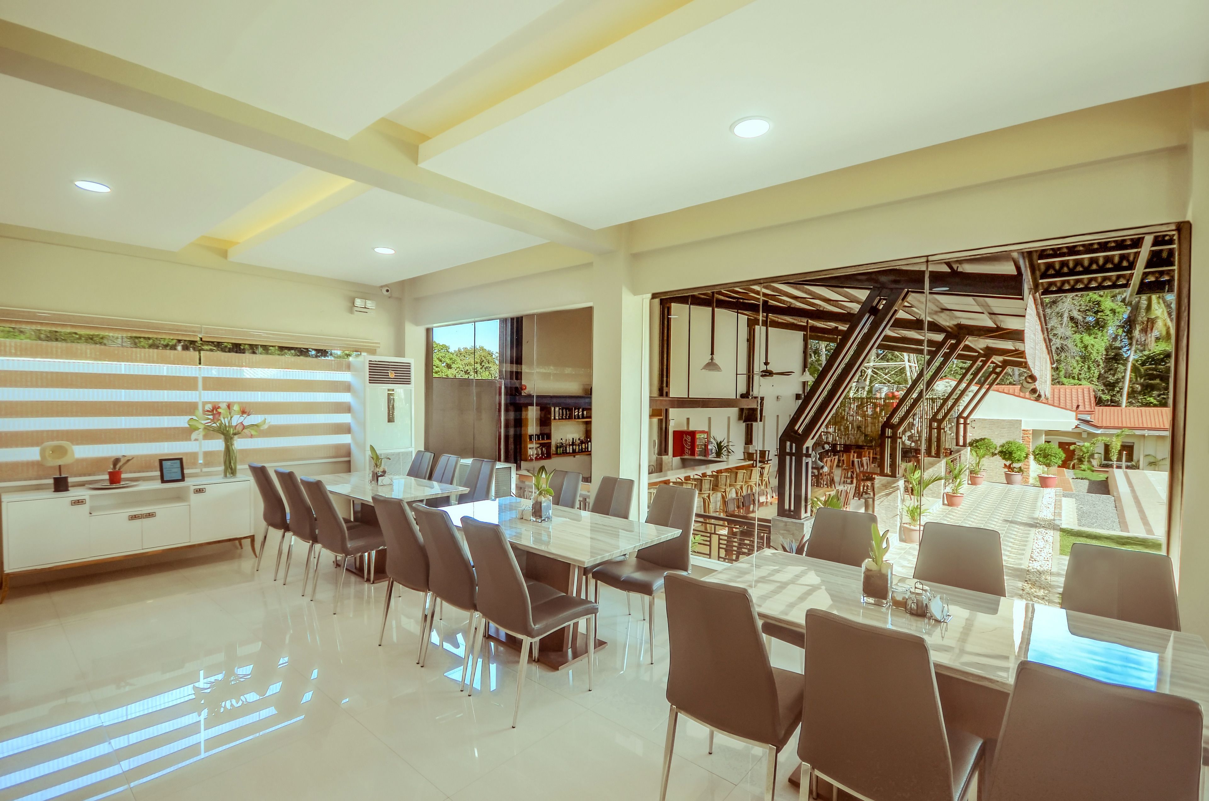 Un comedor amplio con una mesa larga y sillas, una zona de cocina con barra, y una escalera que lleva a una terraza al aire libre.