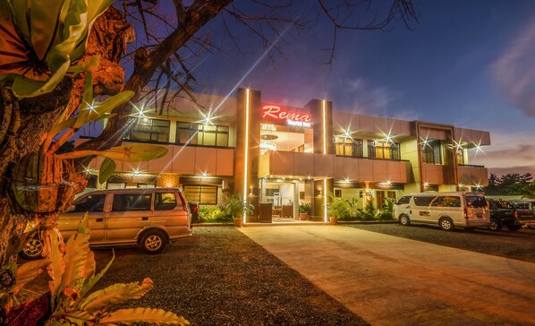 A building with a 'Rema' sign, multiple cars parked in front, and a well-lit entrance.