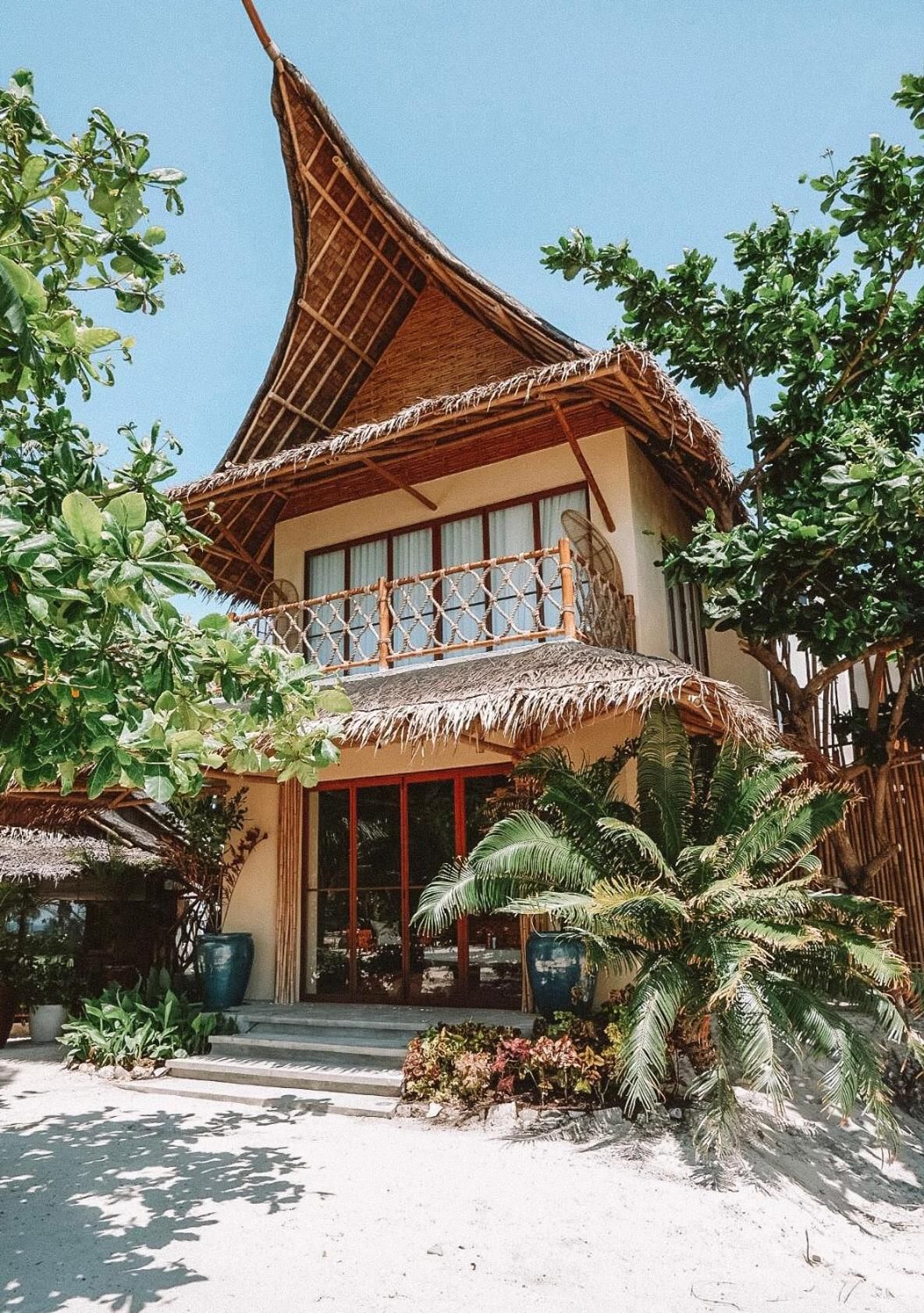 A two-story building with a thatched roof, large windows, and a balcony with a woven railing.