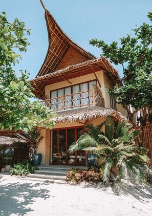 A two-story building with a thatched roof, large windows, and a balcony with a woven railing. - Amihan Beach Cabanas (Santa Fe)