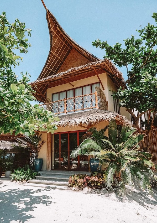 A two-story building with a thatched roof, large windows, and a balcony with a woven railing. - Amihan Beach Cabanas (Santa Fe)