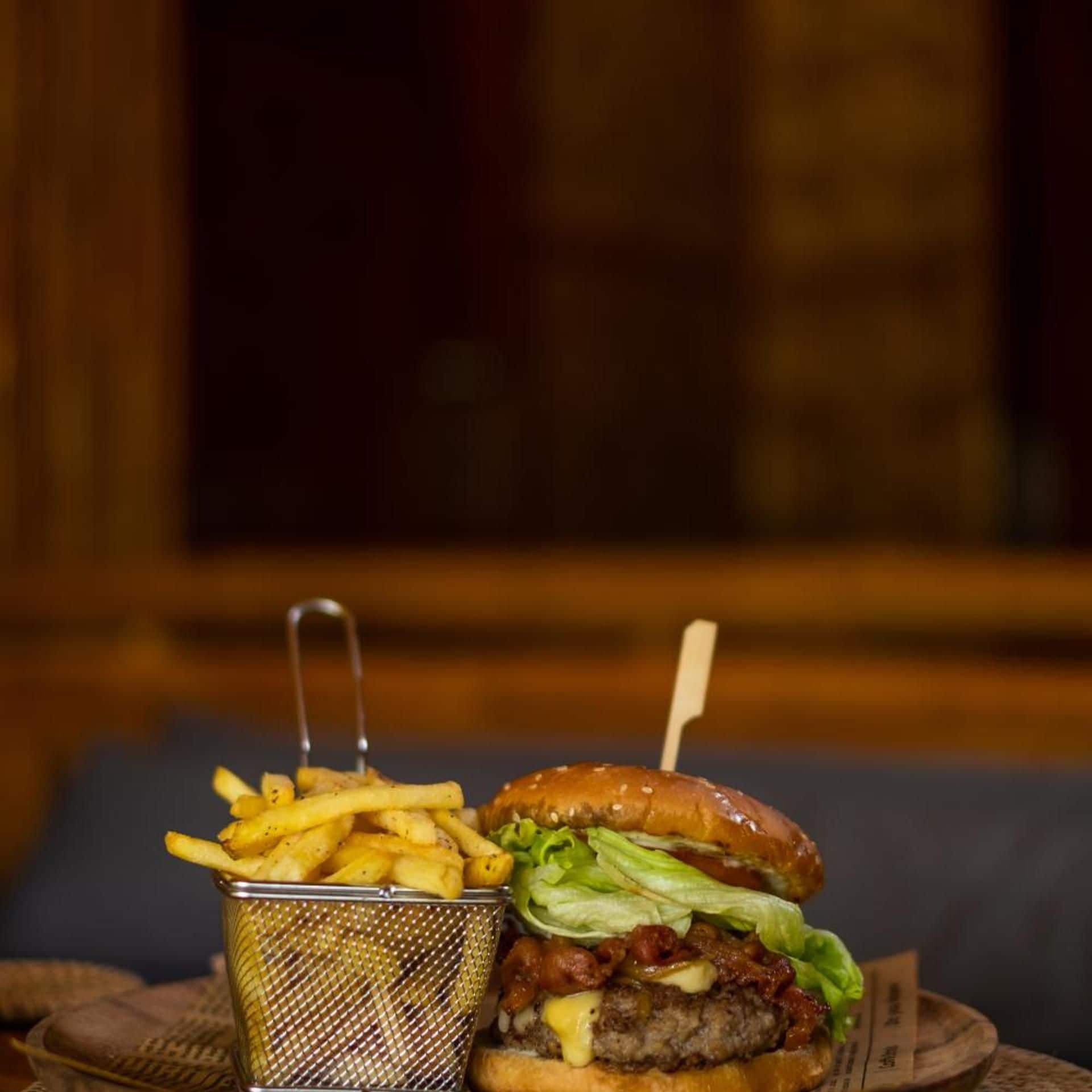 A burger with a bun, lettuce, and a beef patty, accompanied by a basket of French fries.