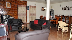 A living room with a black leather sofa, a grey armchair, and a dining area with a wooden table and chairs. - Relaxed Style of Stay (Kandy)