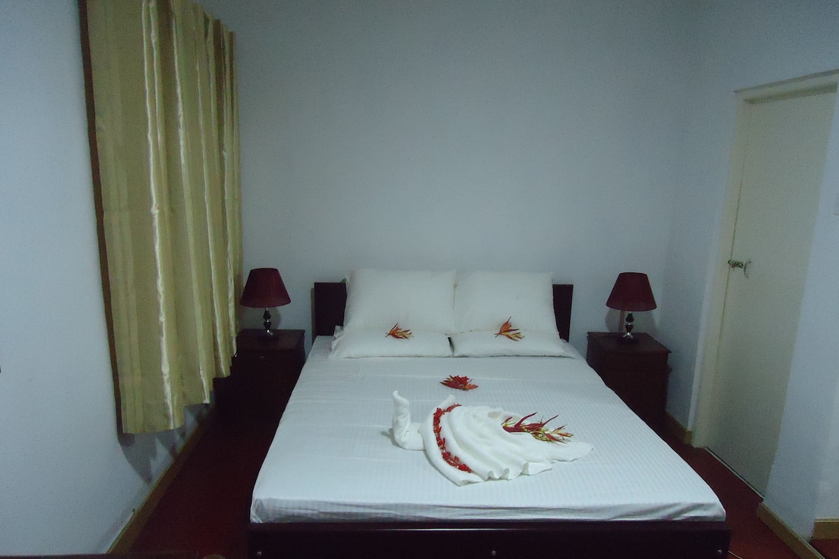 A neatly made bed with white linens and decorative pillows, two bedside lamps, and a wooden headboard.