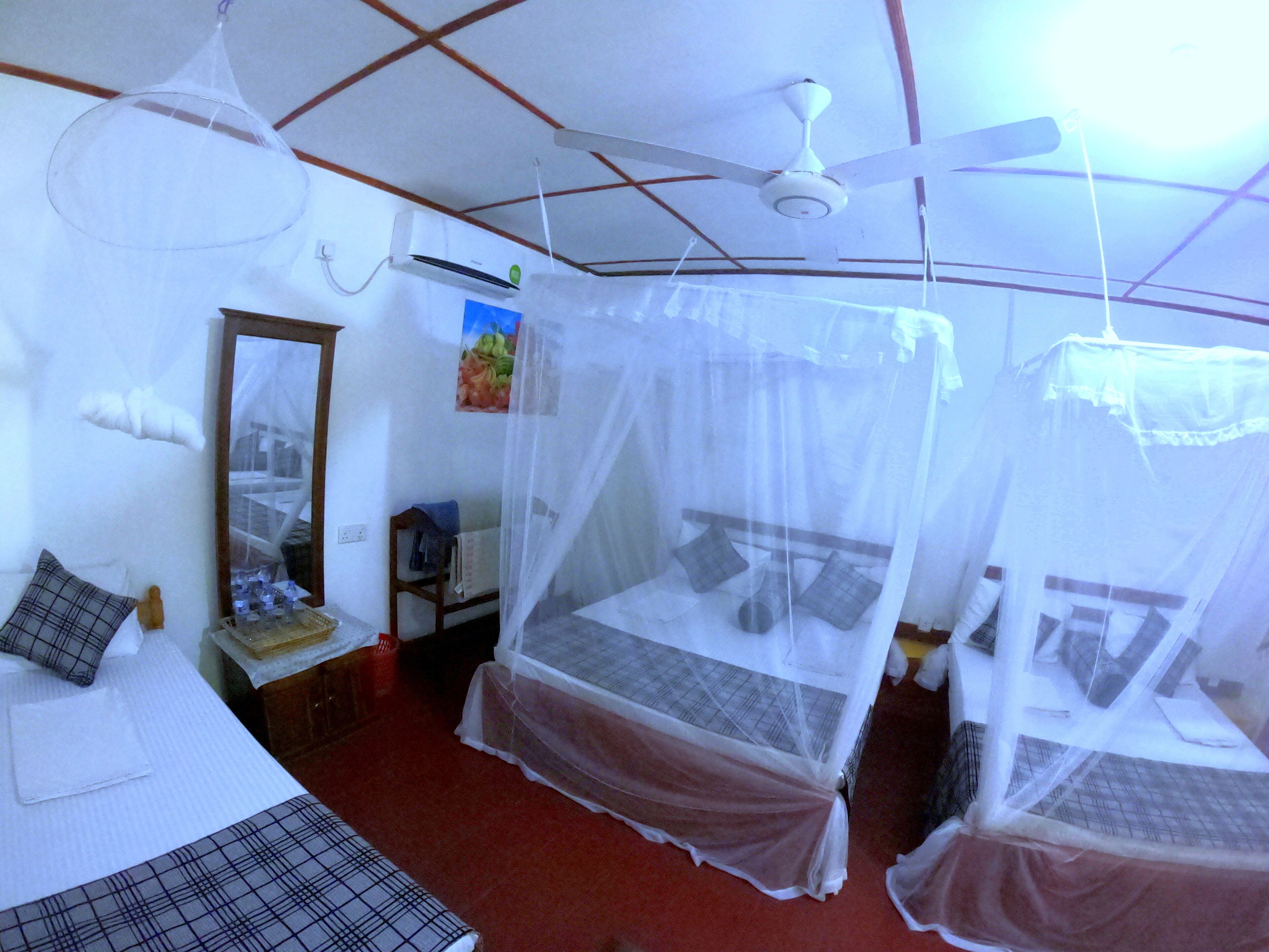 Quarto com duas camas, cada uma com mosquiteiro, ventoinha de teto, ar condicionado e espelho na parede.