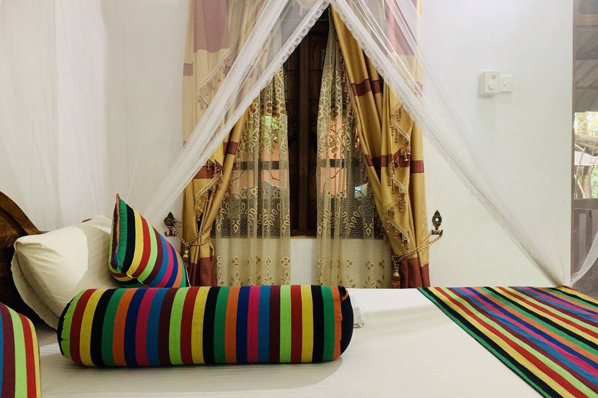 A bedroom with a bed, colorful striped pillows, a canopy, and patterned curtains.