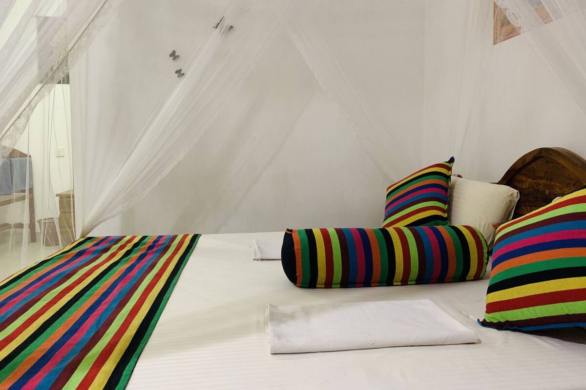 A tent-style room with a bed, colorful striped pillows, and a white canopy.