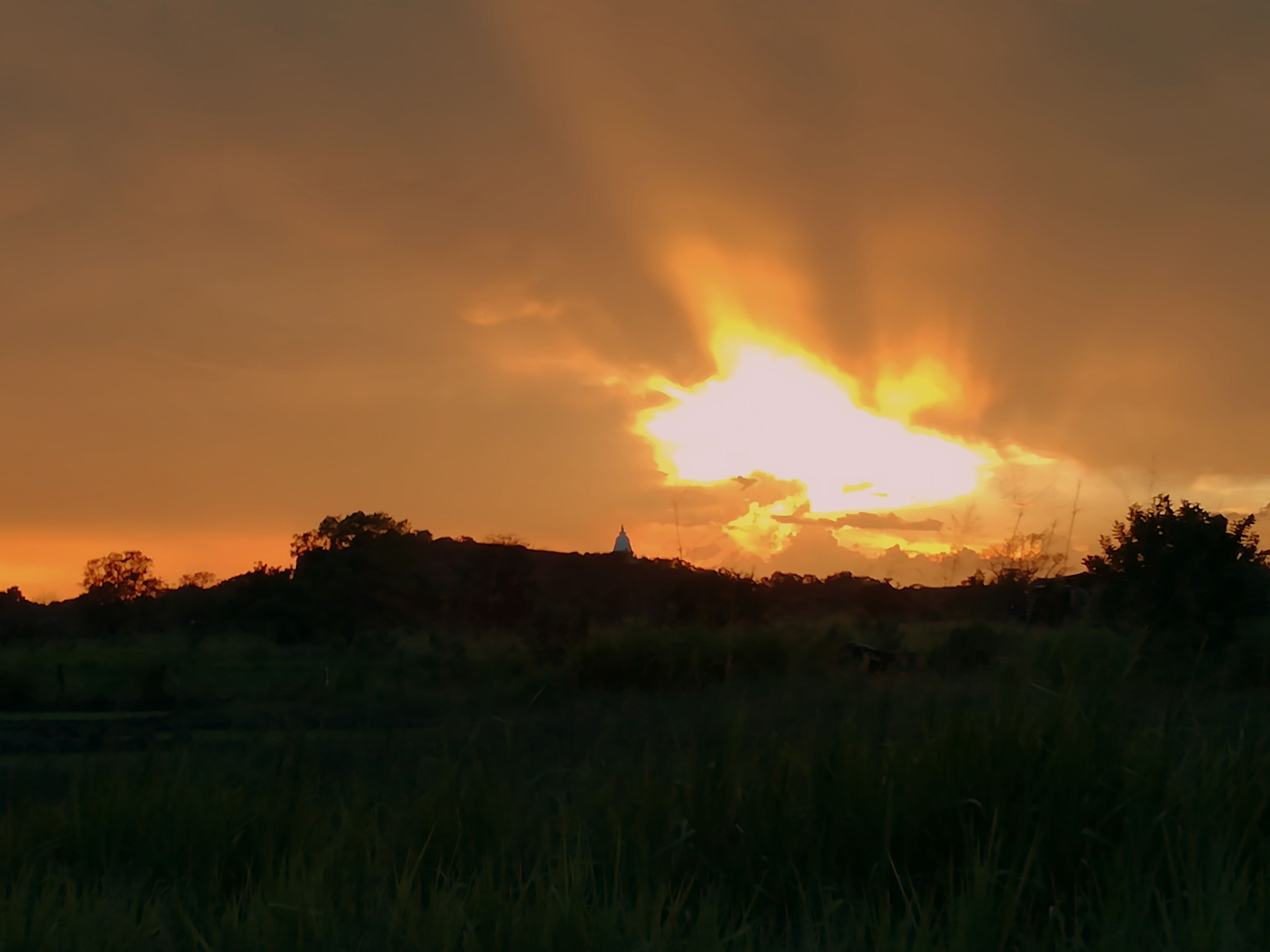 Atardecer sobre un campo cubierto de hierba con la silueta de un edificio lejano.