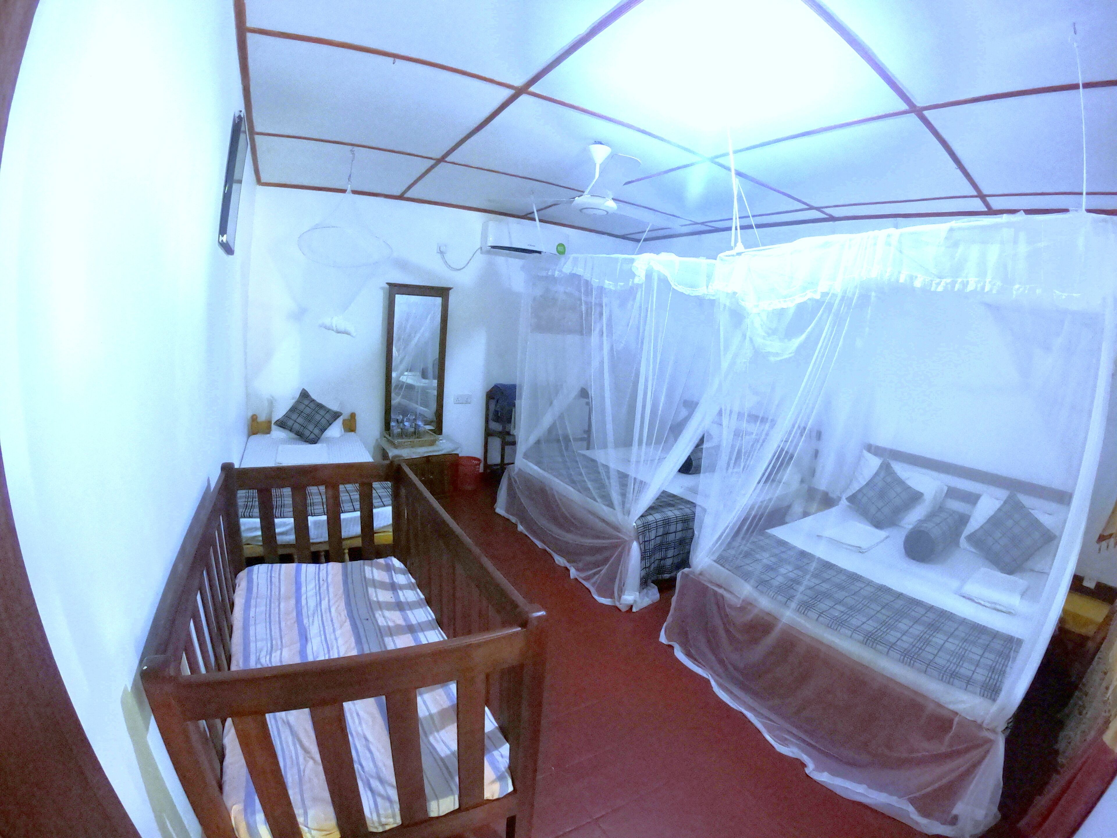 Una habitación con una cuna de madera, una cama con mosquitero, un espejo y un ventilador de techo.