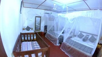 Una habitación con una cuna de madera, una cama con mosquitero, un espejo y un ventilador de techo.