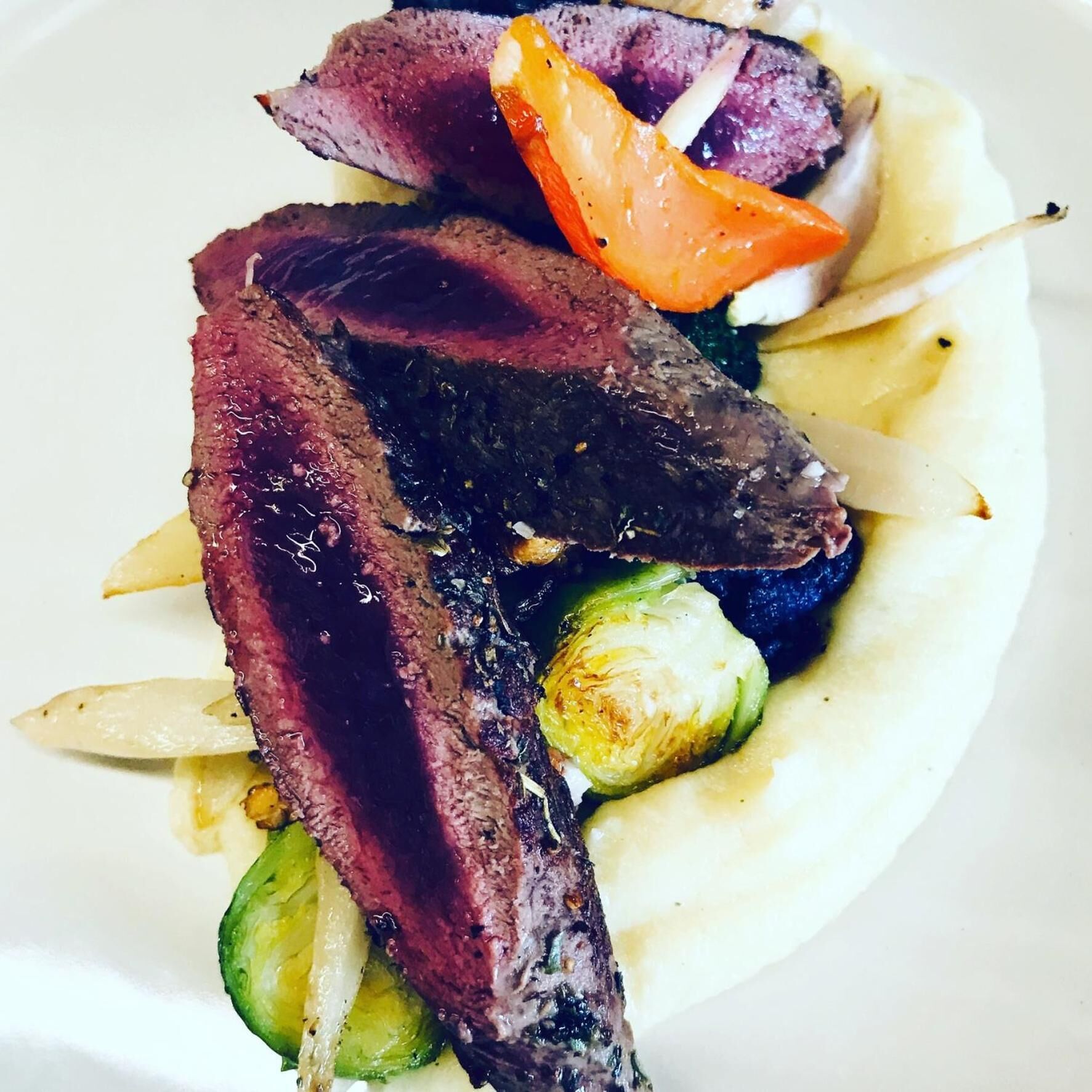 Un plato con tiras de carne, verduras asadas y una base cremosa.