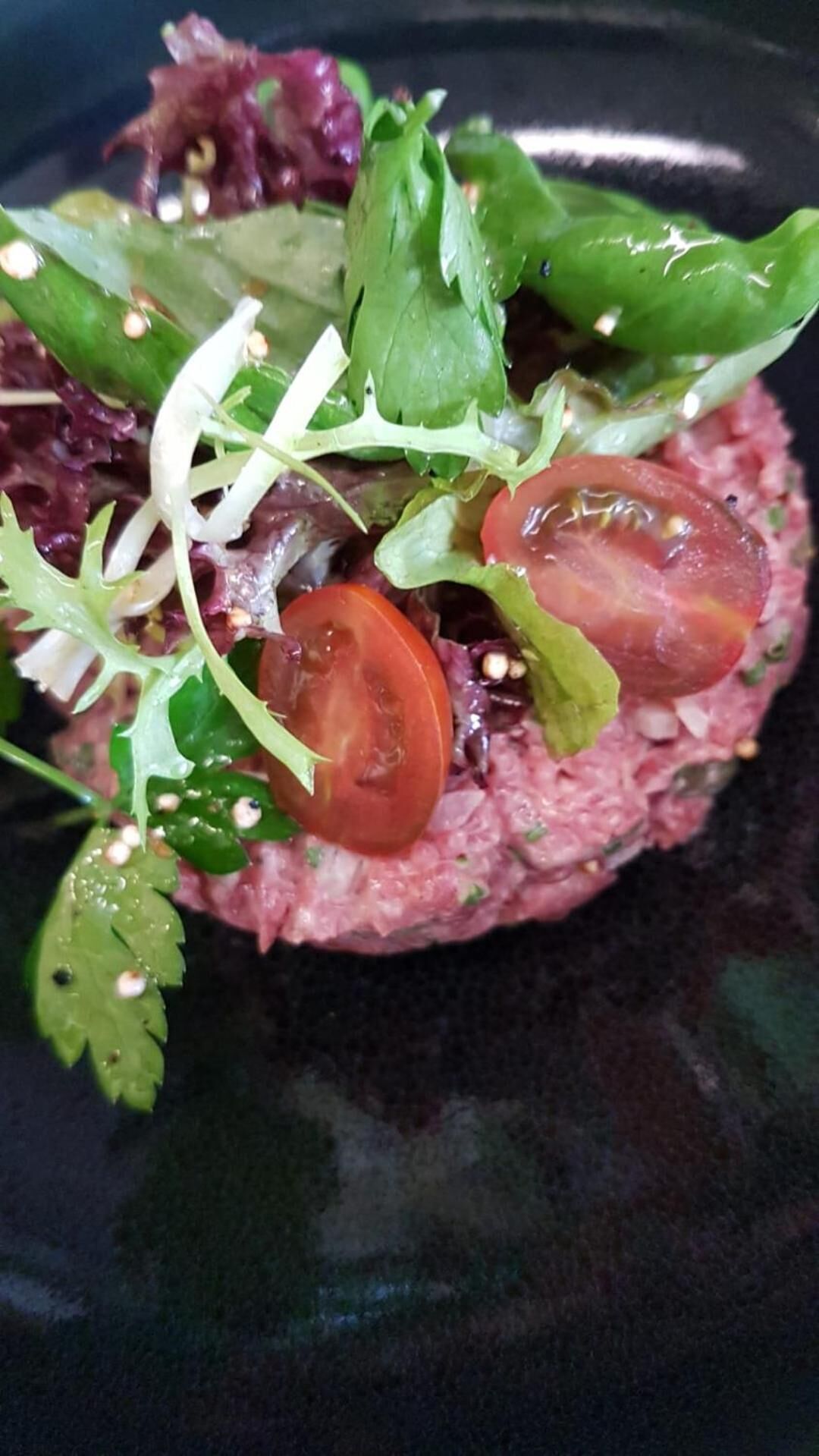 Ein Nahblick auf ein Gericht mit einer Fleischbeilage, garniert mit verschiedenen Blattsalaten und Tomatenscheiben.
