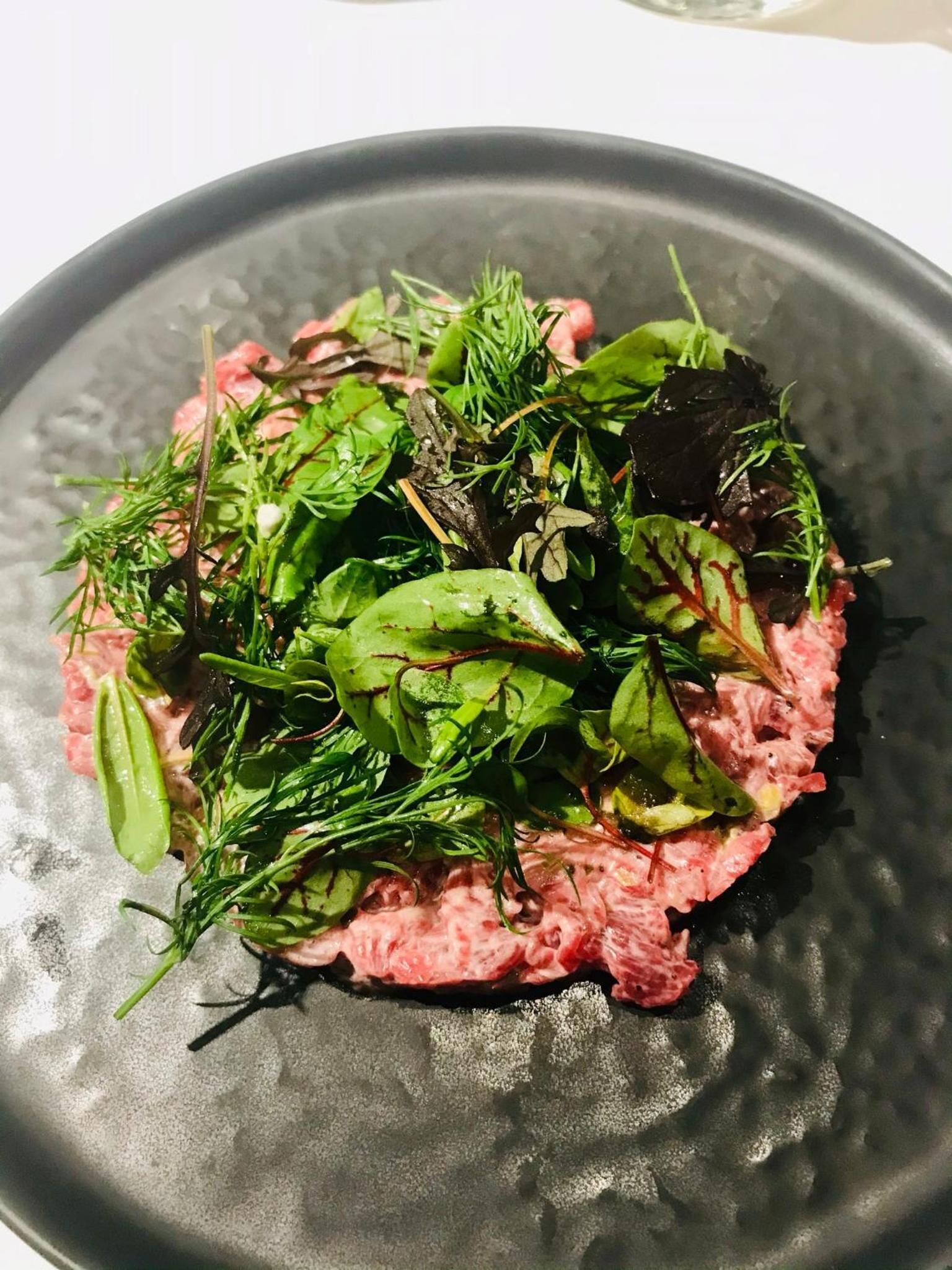 A plate of food with a variety of greens and a pinkish base, possibly a meat dish.