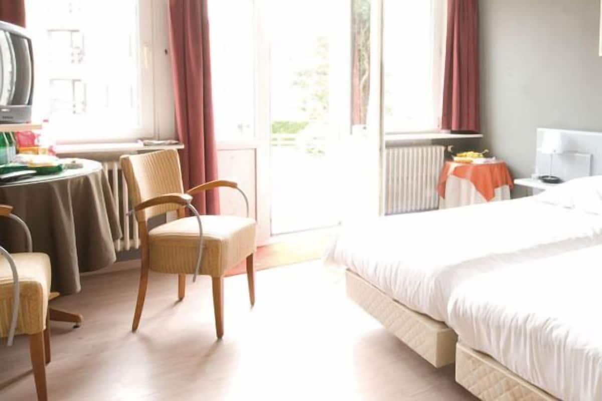 Ein Hotelzimmer mit Bett, Schreibtisch, Stuhl und einem Fenster mit Vorhängen.