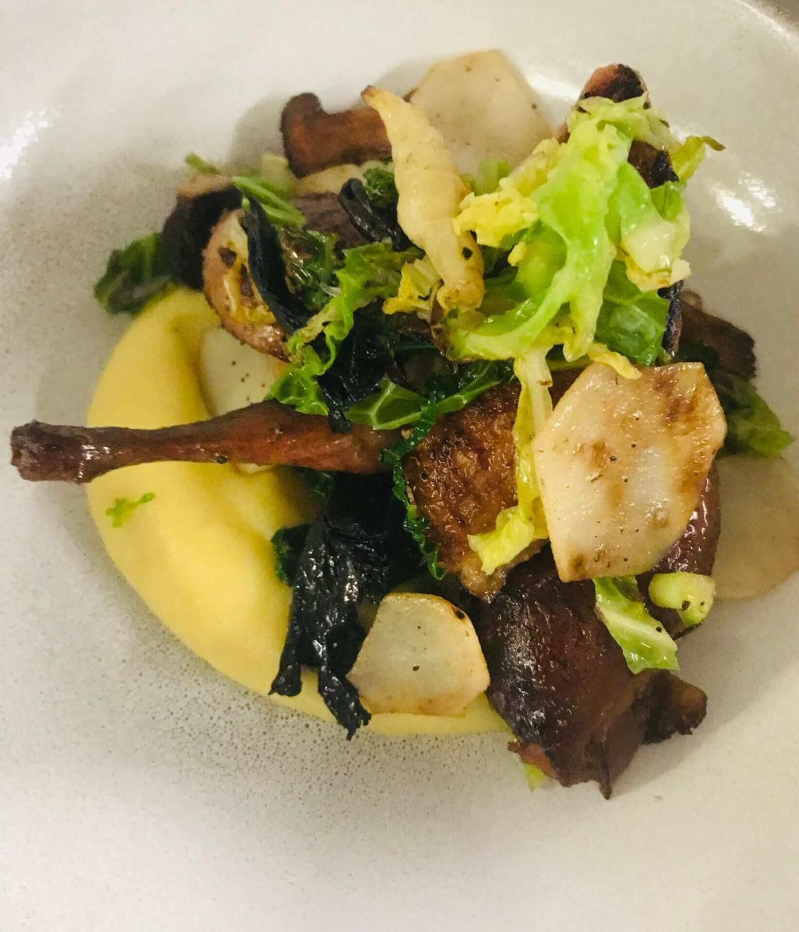 Un plato de comida con diversos ingredientes, incluyendo verduras, setas y un trozo de carne, servido en un plato blanco.