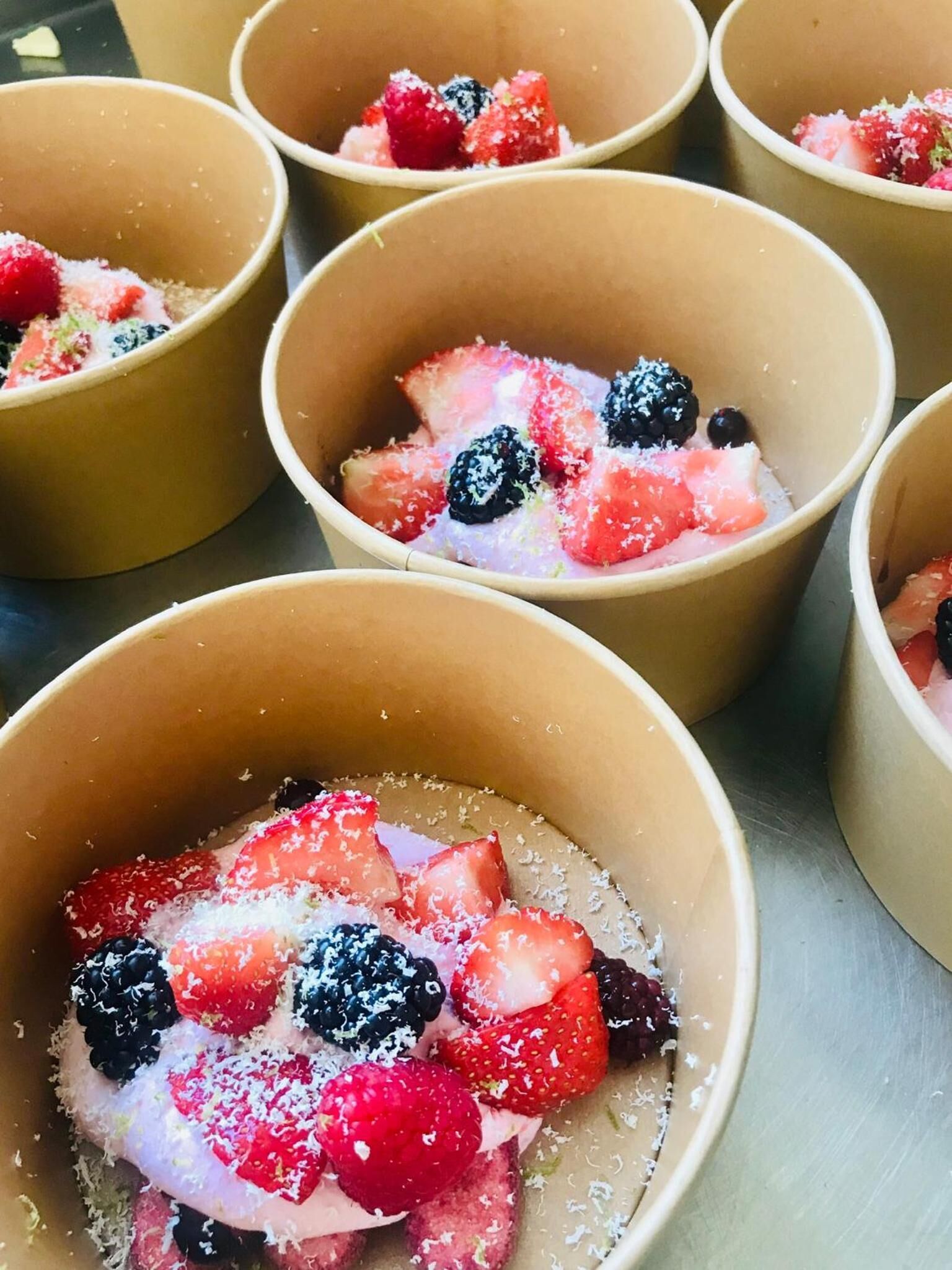Varias fuentes con un postre de fresas, zarzamoras y coco rallado.