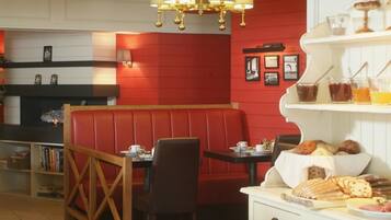 A cozy restaurant with a red booth seating area, a chandelier, and a variety of baked goods displayed on shelves.
