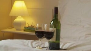 A bed with two wine glasses and a bottle of wine, a lamp, and a small table with a plant. - Hotel Internos (De Haan)