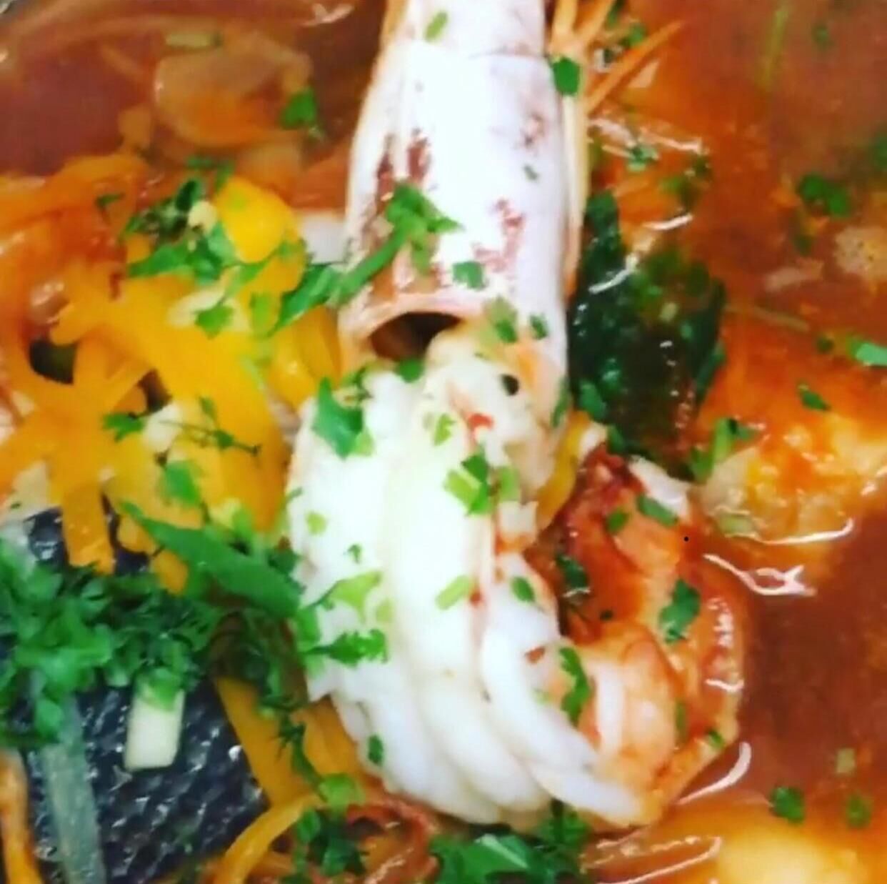 Een visgerecht met garnalen, gele courgette en kruiden in bouillon.