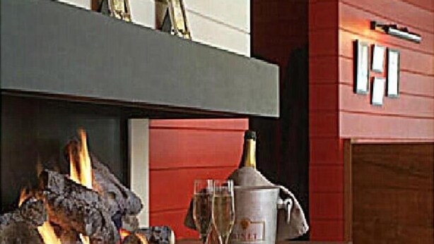 A fireplace with logs, a bottle of champagne, and two glasses on a counter. - Hotel Internos (De Haan)