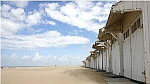 A row of white beachside buildings with a sandy beach and a clear sky. - Hotel Internos (De Haan)