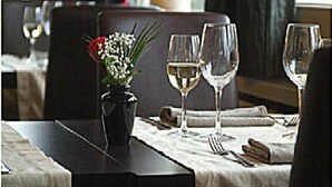 A dining table set with wine glasses, a vase with flowers, and cutlery. - Hotel Internos (De Haan)