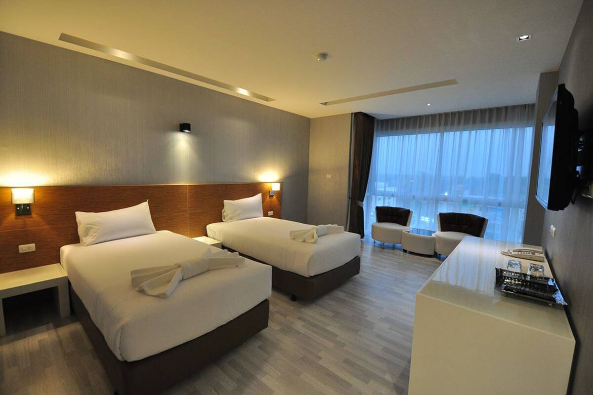 Quarto de hotel com duas camas, uma escrivaninha, uma cadeira e uma televisão na parede.