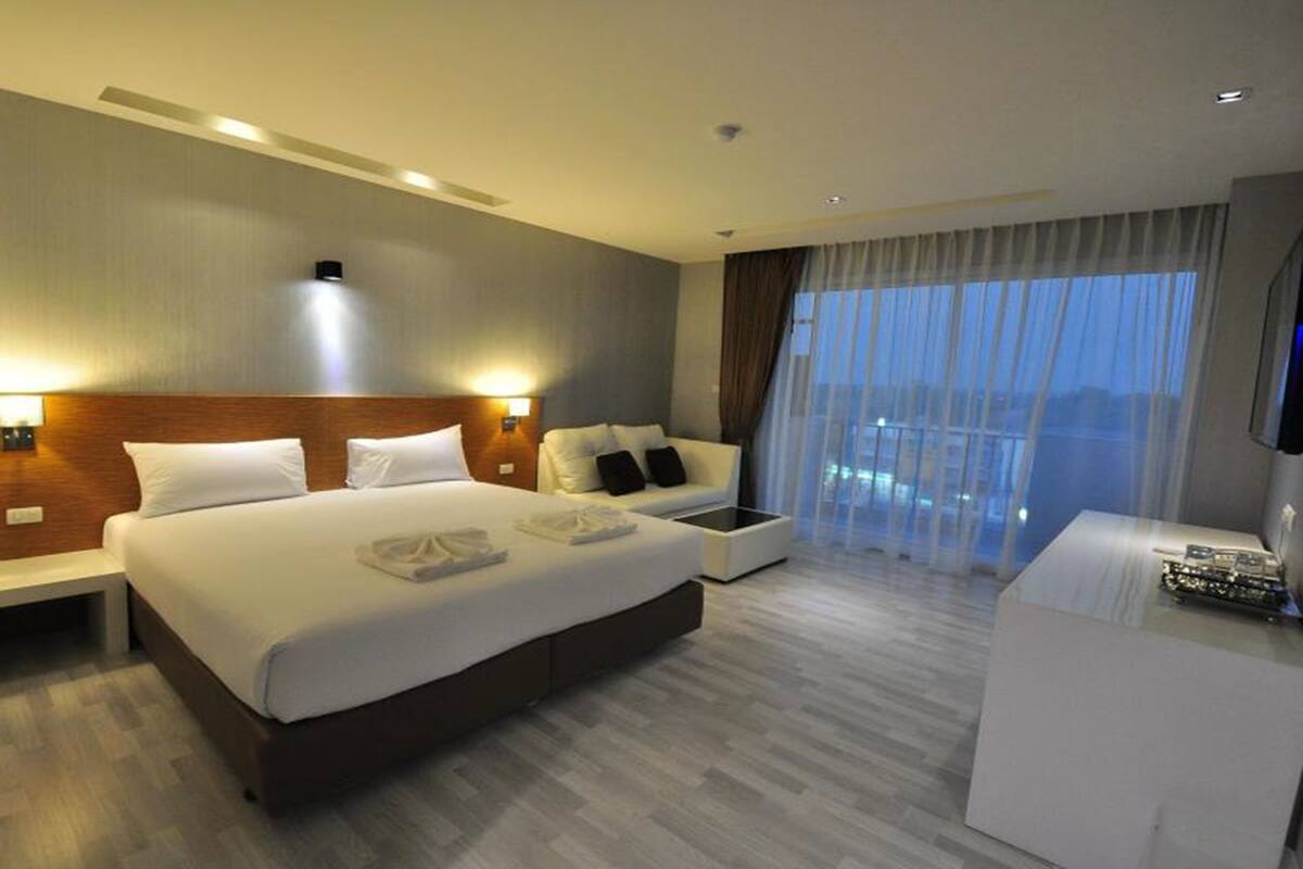 Quarto de hotel moderno com uma cama grande, mesas de cabeceira, escrivaninha e vista da cidade através de amplas janelas.