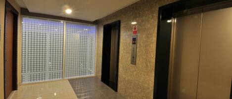 A modern elevator area with a polished floor, a control panel, and a door with a safety sign.