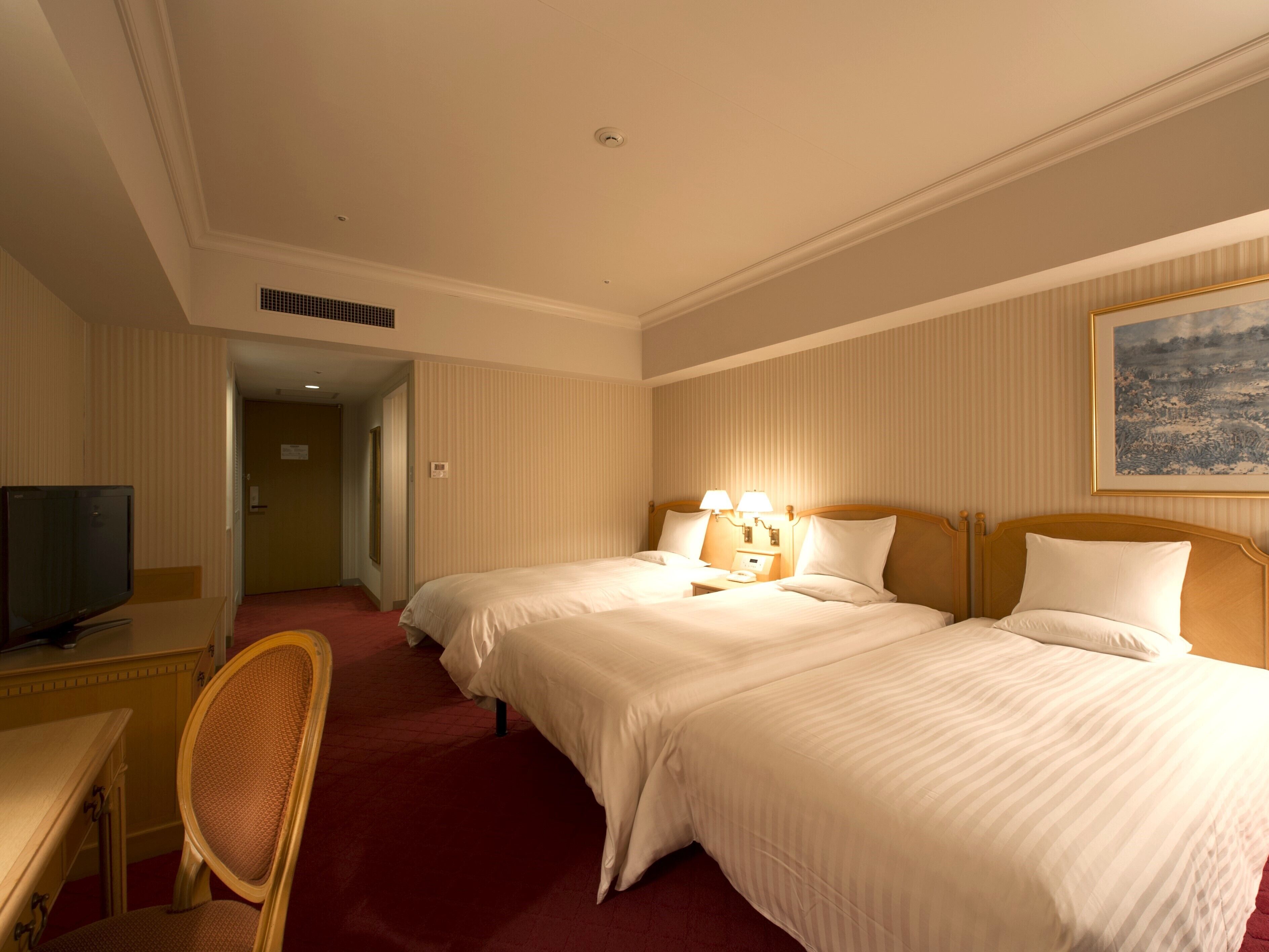 A hotel room with two beds, a desk with a television, and a chair.
