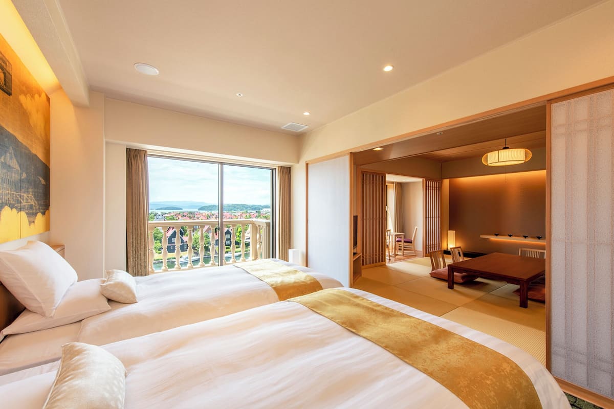 Habitación de hotel con dos camas, un balcón con vistas, zona de comedor y una puerta corrediza que da a otra habitación.